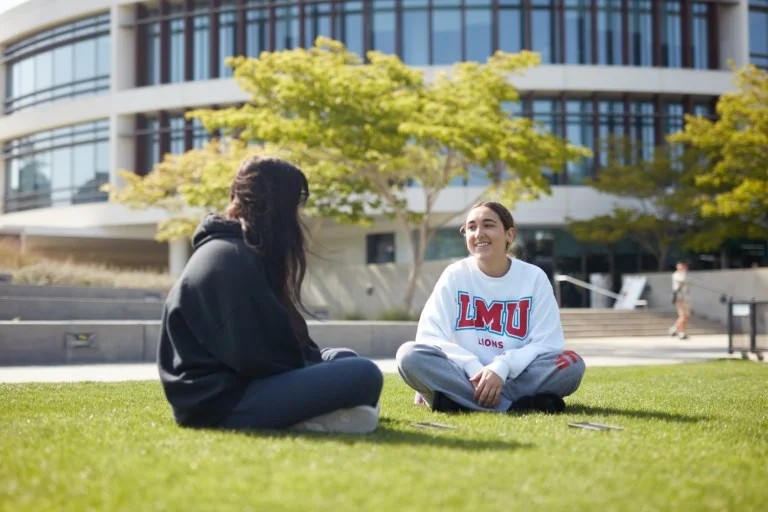 two students sitting on lawn outside library