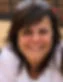 Smiling woman with dark hair wearing sunglasses on her head. Background shows a wooden fence and seating area in daylight.