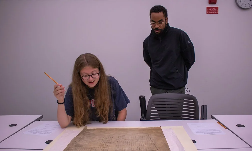 student looking at archival object while faculty looks over her shoulder